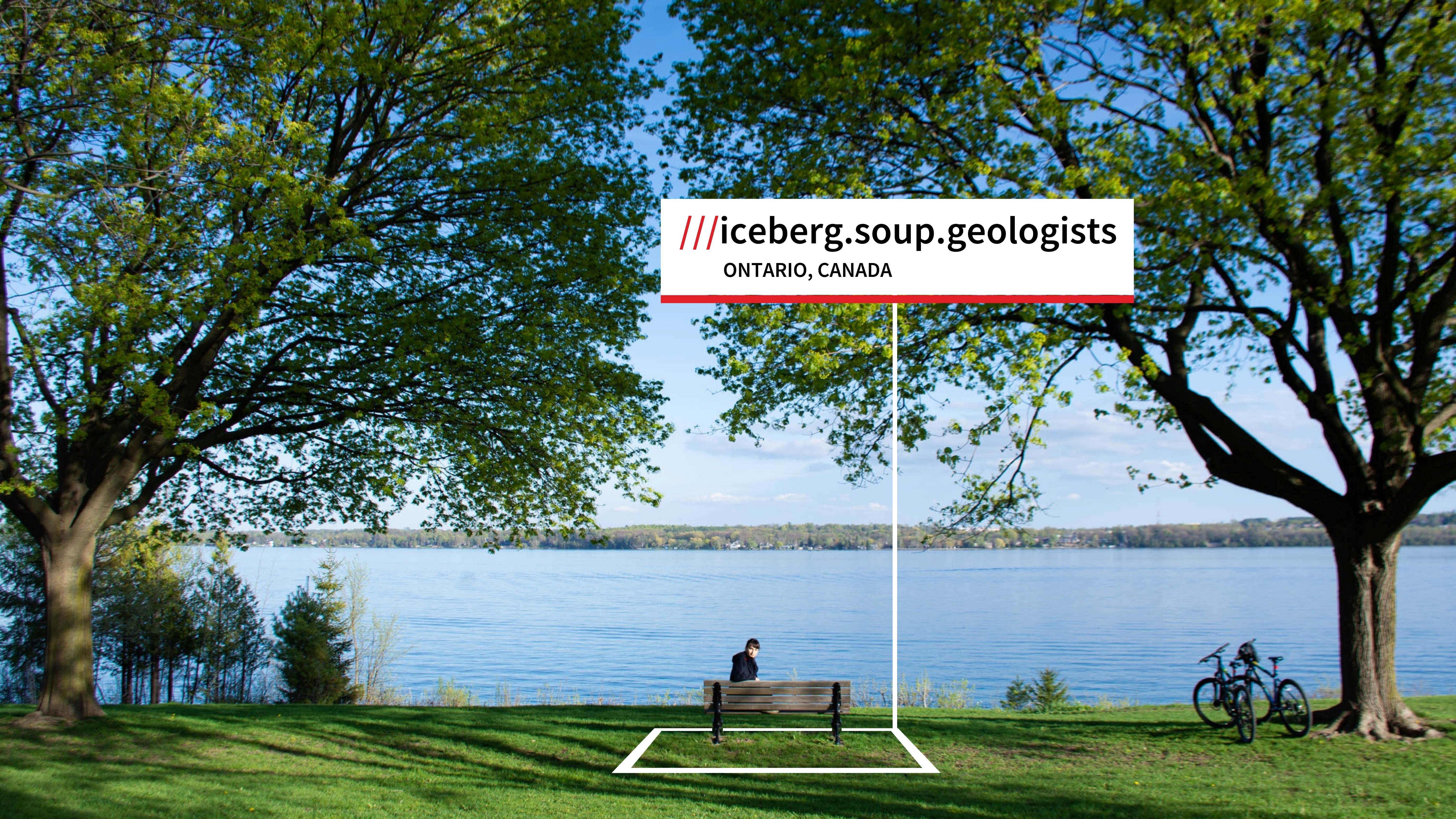 Person sitting on a park bench in front of water with a bicycle and trees with a box that sys iceberg.soup.geologist Ontario, Canada