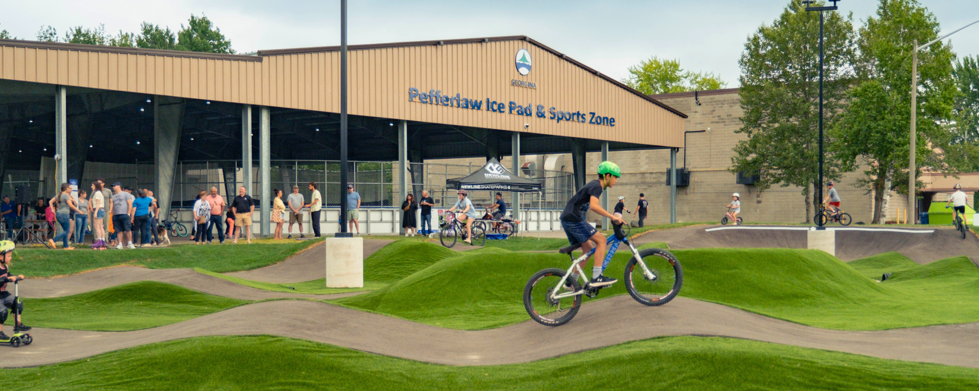 children on bikes and scooters on a concrete pump track with hills